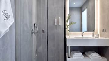 A modern bathroom with a glass shower enclosure, a white sink with a mirror above it, and neatly folded towels on a shelf.