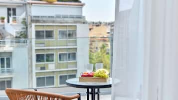 A balcony with a wicker chair, a round table with fruit and glasses, and a view of a building with balconies.