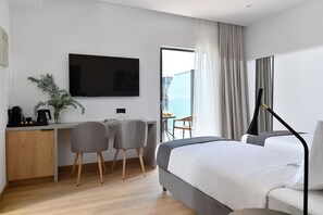 A hotel room with a bed, a desk with two chairs, a TV, and a view of the sea. - Acropolis Lumina (Athens)
