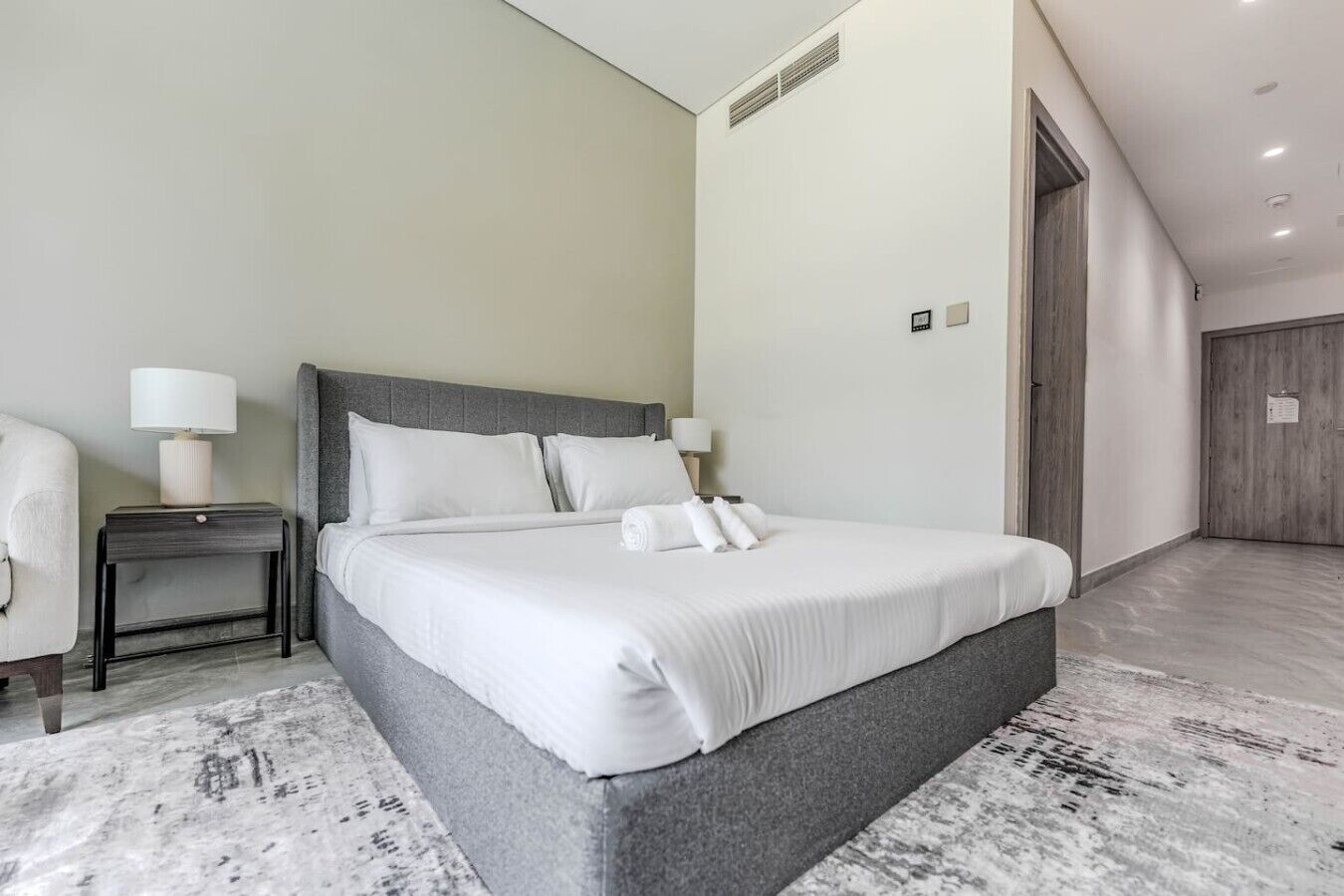 Ein modernes Hotelzimmer mit einem großen Bett, einem Nachttisch, einer Lampe und einer Holztür.