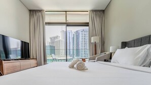 A hotel room with a bed, a TV, a lamp, and a view of tall buildings. - HAVN - Studio in Peninsula 2, Business Bay (Dubai)