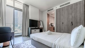 A modern hotel room with a bed, a TV, a desk, and a view of the city. - HAVN - Modern Studio in Peninsula, Business Bay (Dubai)