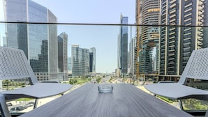 A modern hotel room with a large window offering a city view, a wooden table, and two white chairs. - HAVN - Modern Studio in Peninsula, Business Bay (Dubai)