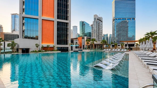 A swimming pool with lounge chairs and umbrellas, surrounded by modern buildings. - HAVN - Modern Studio in Peninsula, Business Bay (Dubai)