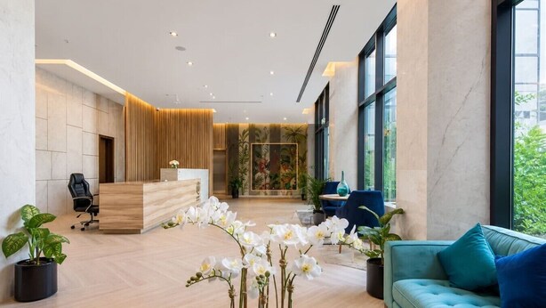 Un espace d’accueil moderne avec un comptoir de réception en bois, un canapé bleu et des plantes en pot.