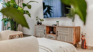 Un salon moderne avec une grande télévision, un fauteuil en rotin, un meuble en bois à motifs et une plante en pot.