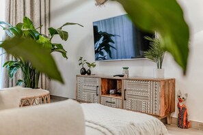 Ein modernes Wohnzimmer mit großem Fernseher, einem Rattan-Sessel, einer Holzkabine mit Muster und einer Topfpflanze.