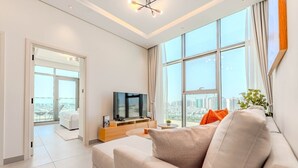 Un soggiorno moderno con una grande TV, un divano e vista sulla città attraverso ampie finestre.