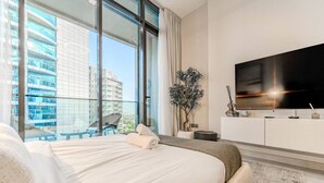 Una habitación de hotel moderna con una cama grande, televisor, balcón con vista a la ciudad y una planta en maceta.