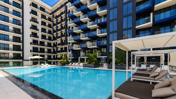 Ein modernes Hotel mit Schwimmbad, Liegestühlen und einem überdachten Bereich.