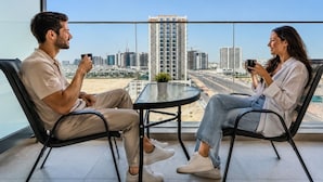 Two people seated at a table with a city view, on a balcony with a glass railing. - HAVN - Studio in PG One, Al Furjan (Dubai)