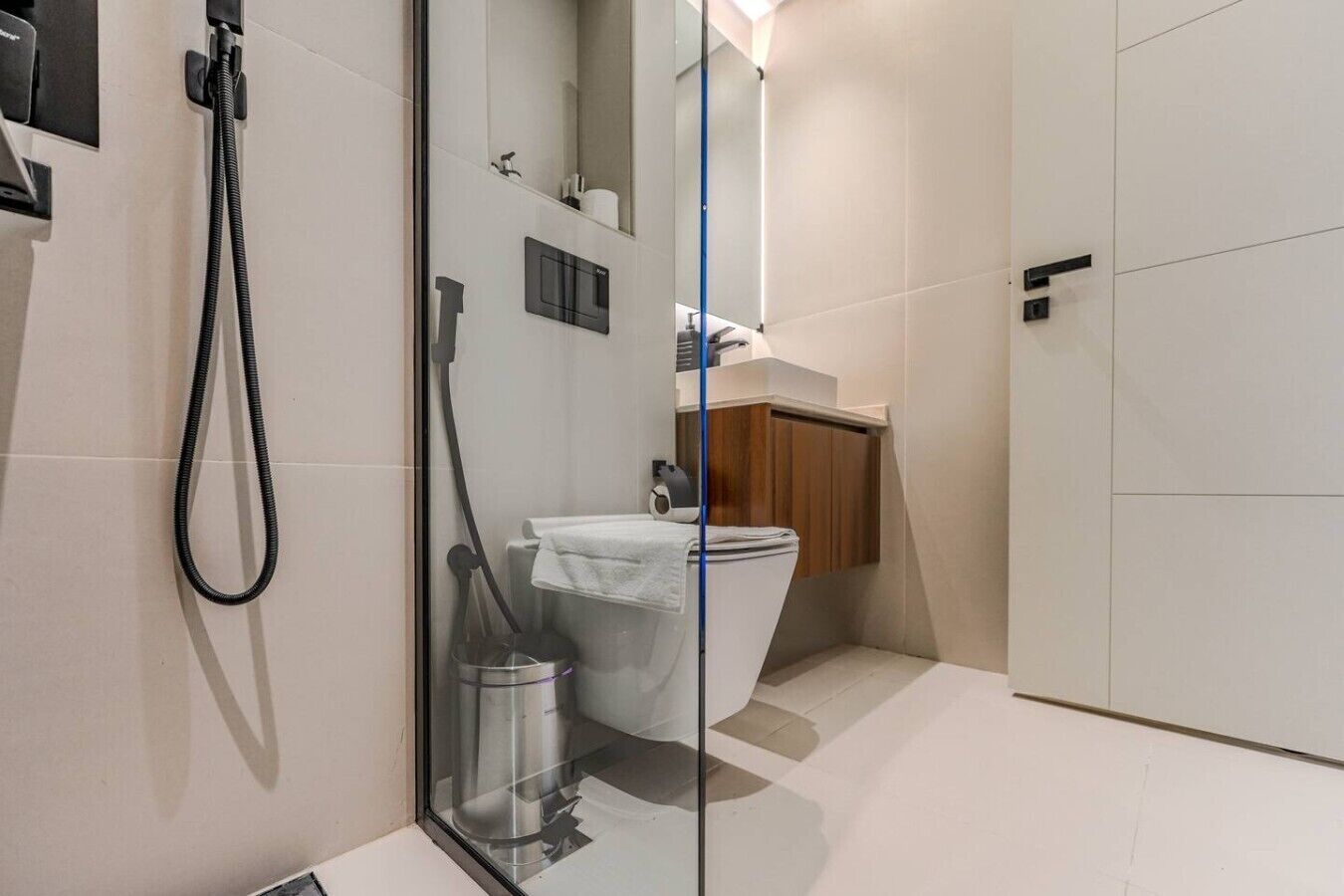 A modern bathroom with a glass shower enclosure, a toilet, and a sink with a wooden cabinet.