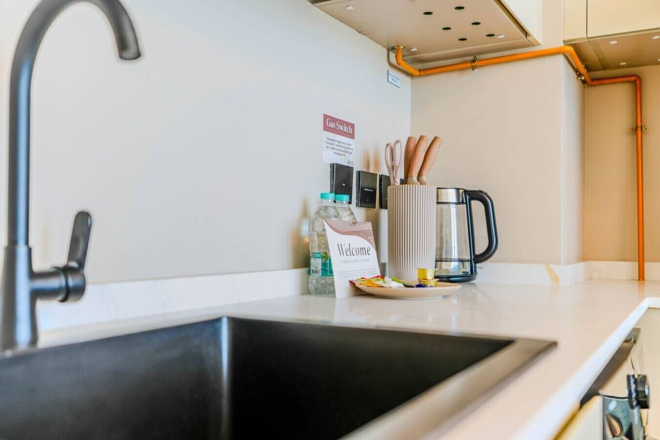 A modern kitchen with a black sink, a coffee maker, and a welcome sign.