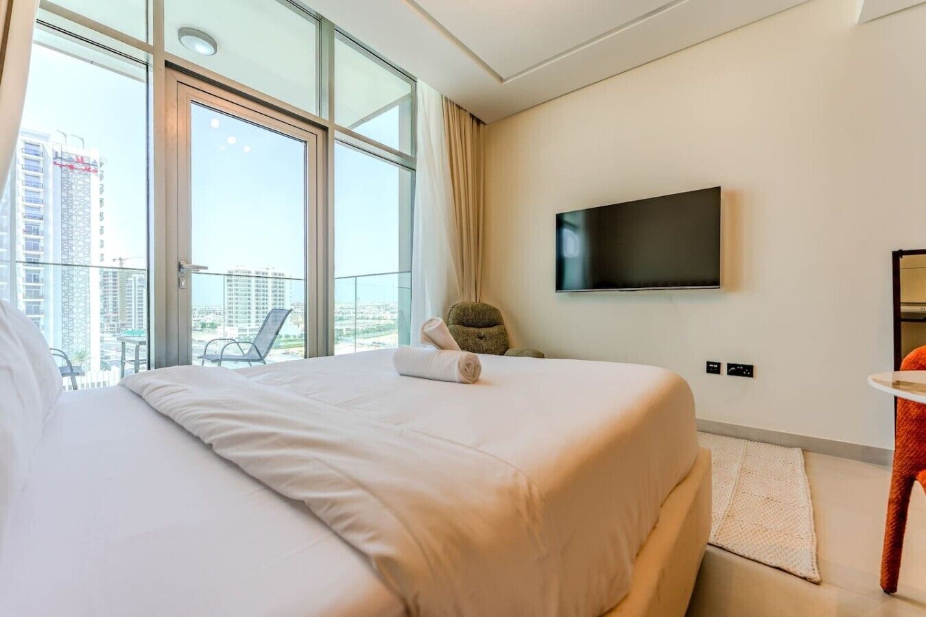 Una camera d'albergo con un letto grande, una TV fissata al muro e un balcone con una sedia.