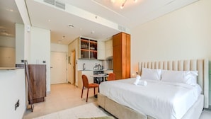 A modern hotel room with a large bed, a small desk, and a kitchenette. - HAVN - Studio in PG One, Al Furjan (Dubai)