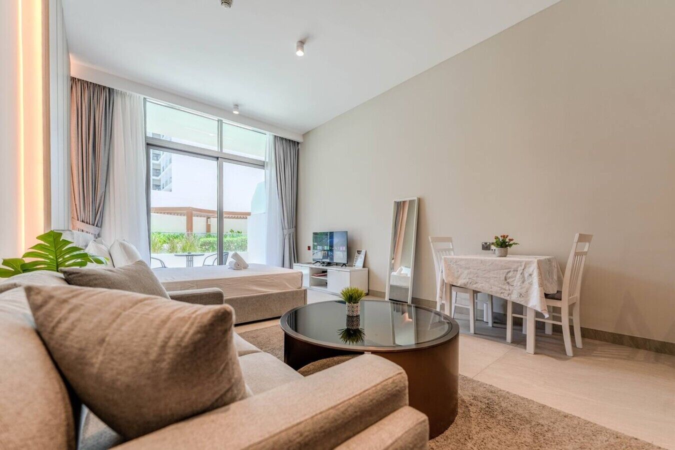 En moderne stue med en sofa, et sofabord i glas, et spisebord med stole, et fladskærms-tv og et stort vindue med gardiner.