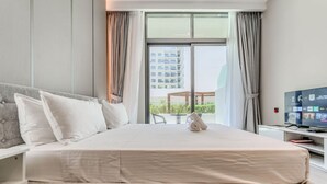 A hotel room with a bed, a TV, a window with curtains, and a view of a building outside. - HAVN - Studio in Stonehenge Residences, JVC (Dubai)