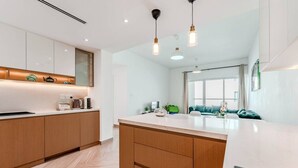 Une cuisine moderne avec des meubles en bois, un îlot central, des luminaires suspendus et une vue sur un espace de vie comprenant un canapé et une fenêtre.