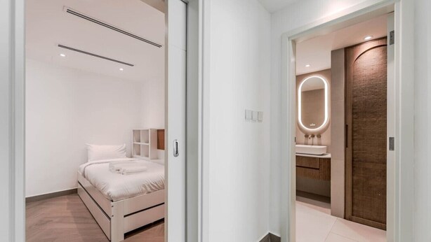 Une chambre moderne avec un lit, des tables de chevet et une salle de bain équipée d’un miroir et d’un lavabo.