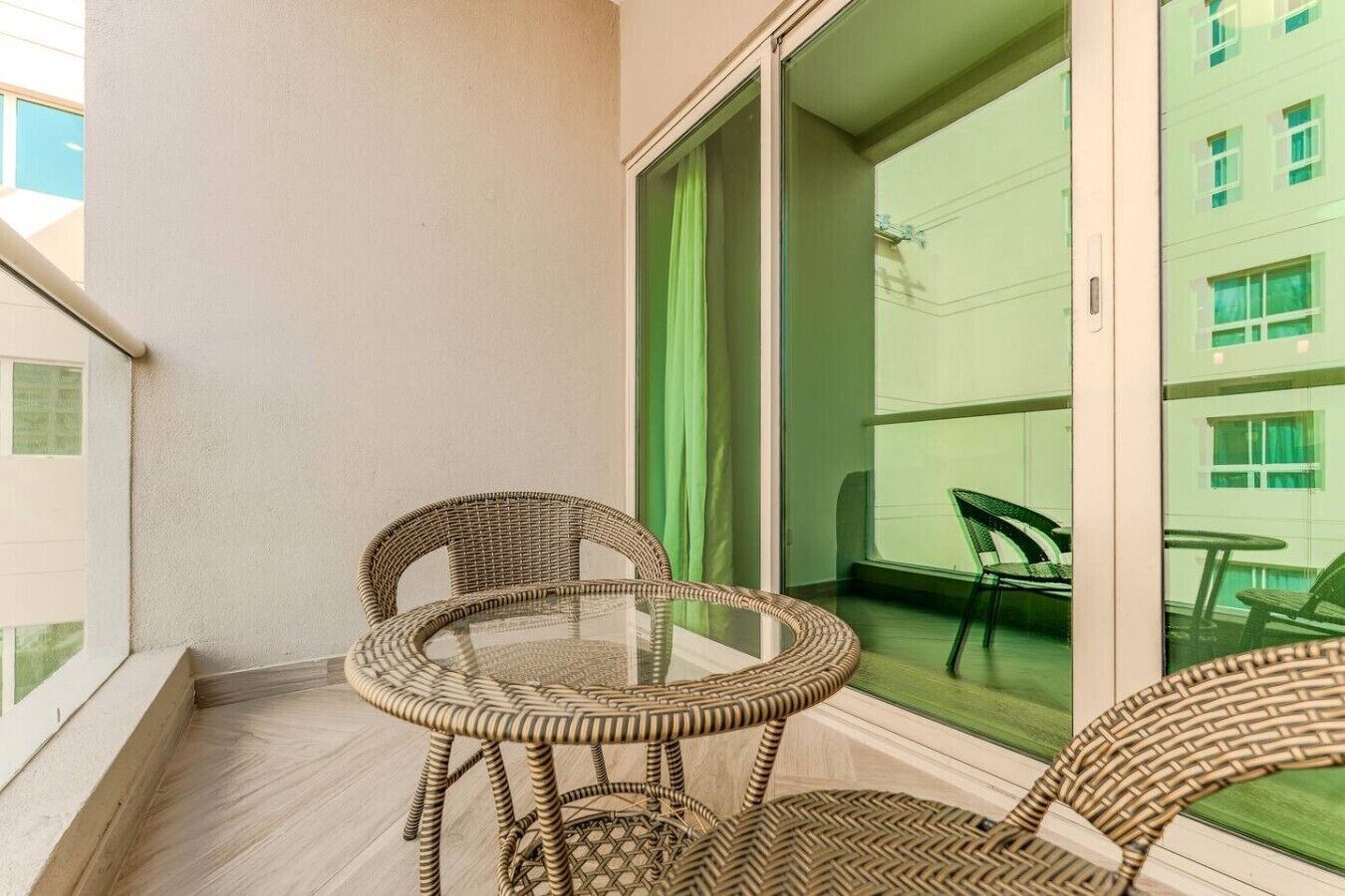 A balcony with wicker furniture, a glass table, and a view of a building with windows.