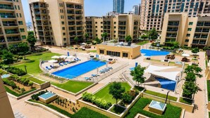 Un immeuble résidentiel à plusieurs étages doté d’une piscine sur le toit, de nombreux balcons et d’un jardin aménagé.