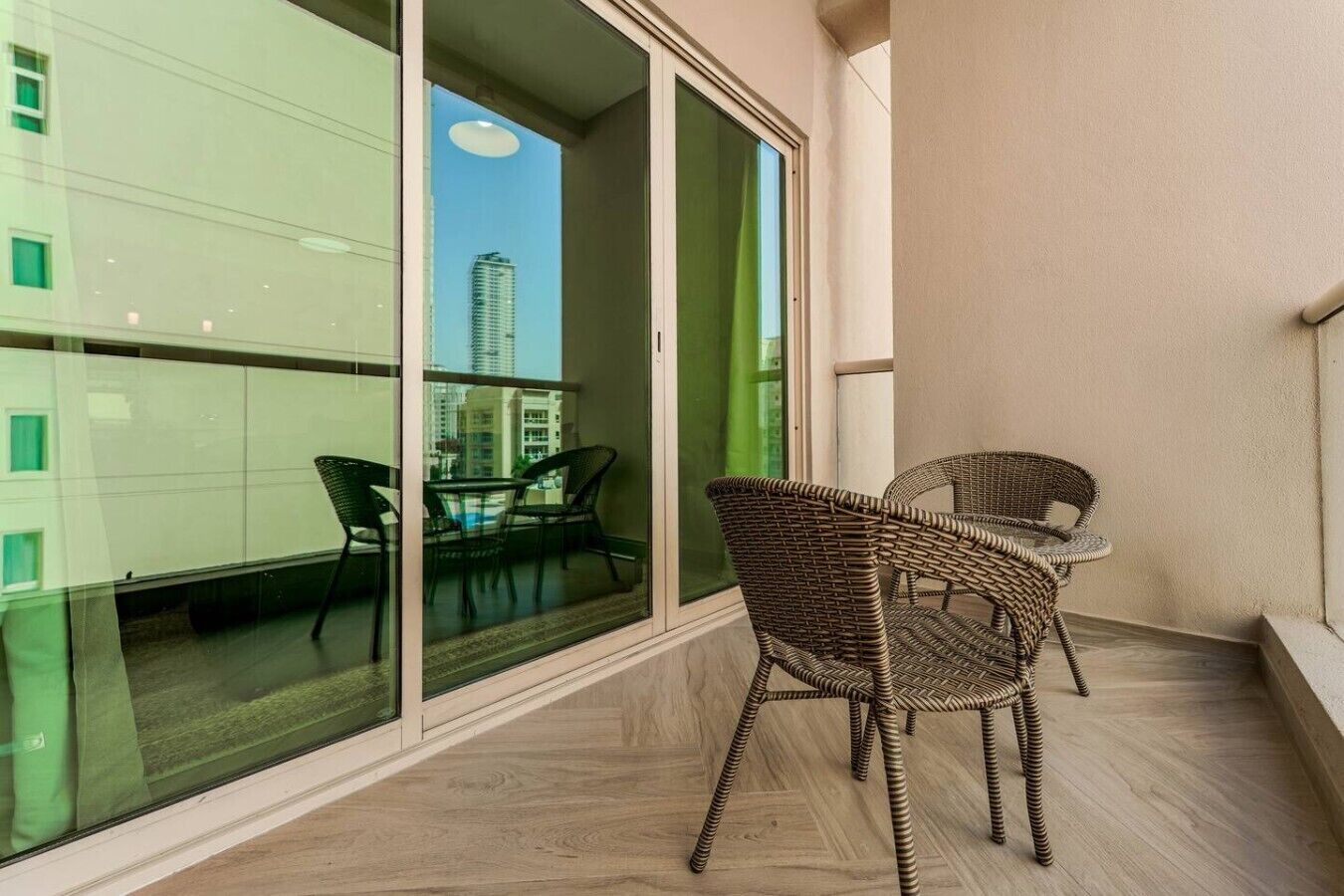 Een balkon met rieten meubilair, een glazen deur en uitzicht op een stadsgezicht.