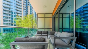 A balcony with modern furniture, large windows, and a view of surrounding buildings. - HAVN - 1 Bedroom in Azure, 5 mins to DMCC metro (Dubai)