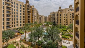 Un immeuble résidentiel de grande hauteur doté de nombreux balcons, d’une cour intérieure avec des palmiers et d’une piscine.