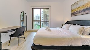 Une chambre à coucher avec un lit, un bureau, une chaise, une fenêtre et un tableau accroché au mur.