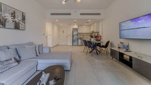 Un salon moderne comprenant un canapé, une table basse, un coin repas avec des chaises, une cuisine et un téléviseur fixé au mur.