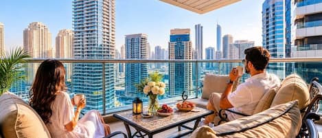 A balcony with two people seated, a table with flowers and food, and a city skyline in the background.
