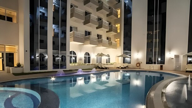 Une piscine au design moderne, entourée d’un immeuble à plusieurs étages doté de balcons.