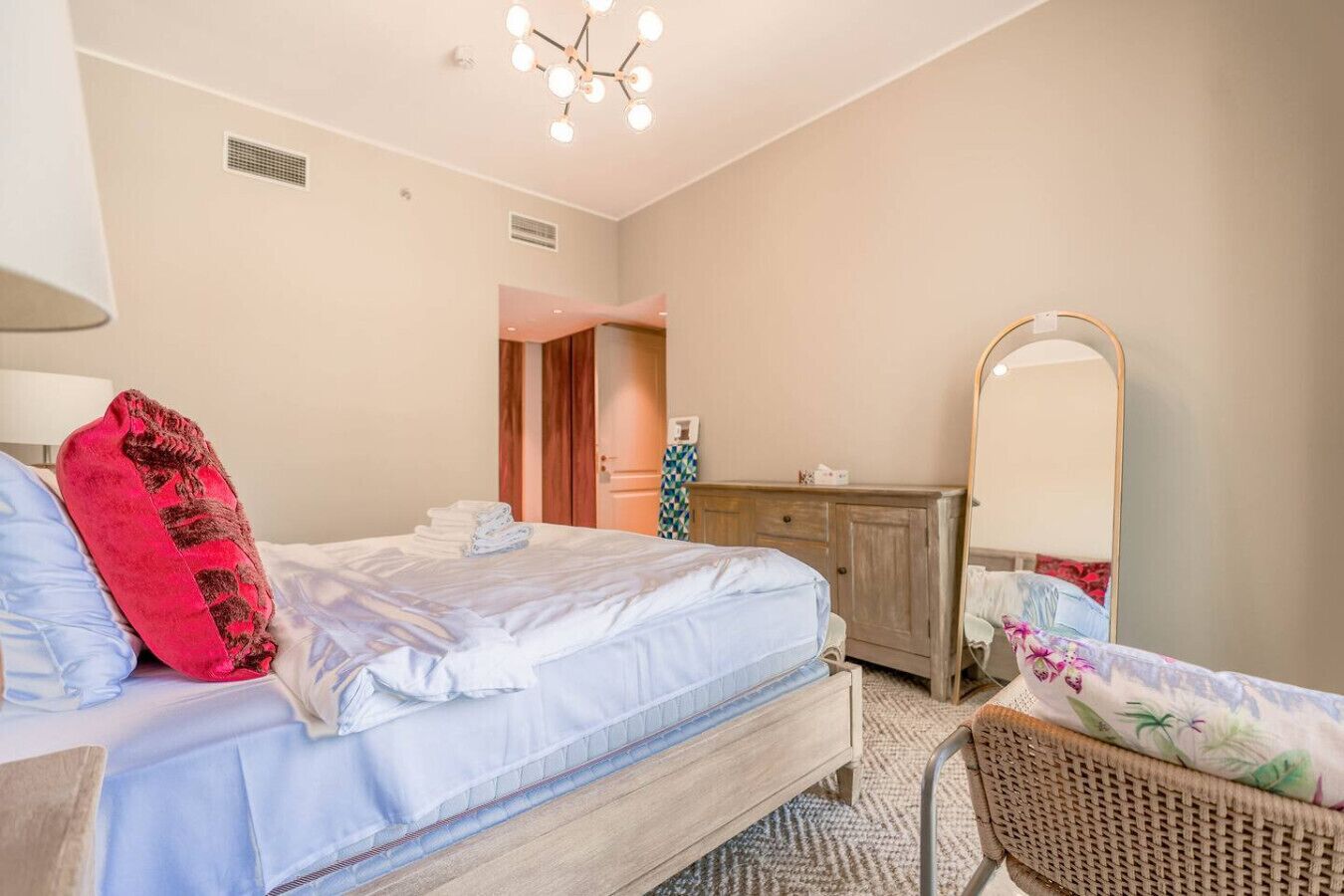 A bedroom with a bed, a dresser, a mirror, a chair, and a door leading to another room.
