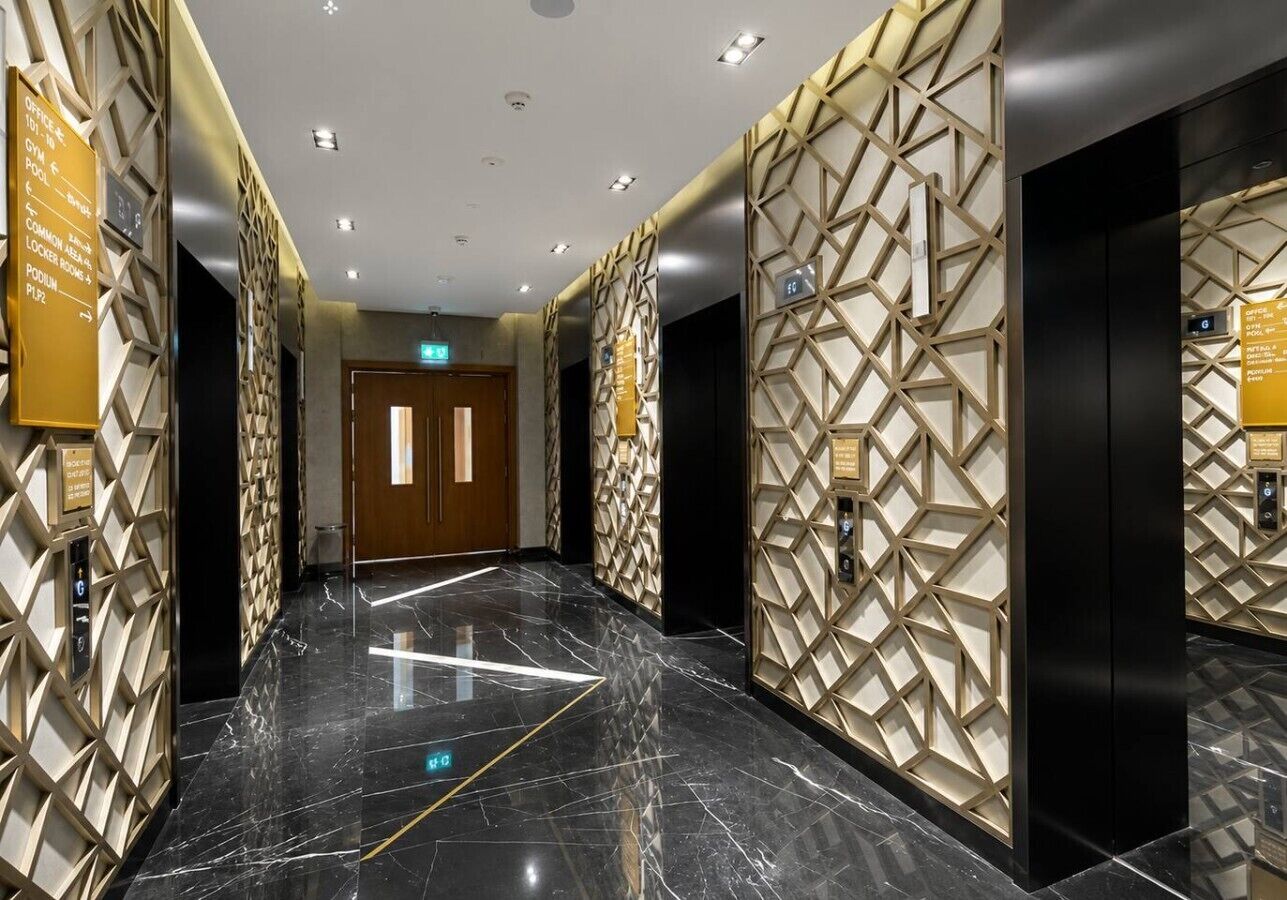 A modern hotel lobby with a marble floor, geometric wall patterns, and directional signs.