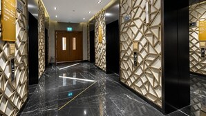 A modern hotel lobby with a marble floor, geometric wall patterns, and directional signs. - HAVN - 2 Bedroom in Aykon Tower, Business bay (Dubai)