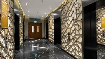A modern hotel lobby with a marble floor, geometric wall patterns, and directional signs.