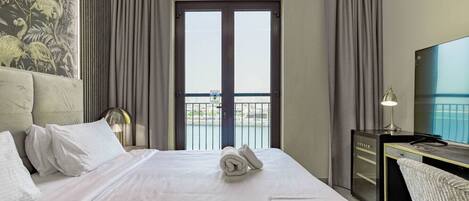 A hotel room with a bed, a desk, a television, and a balcony with a view.