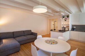 A modern living room with a gray sectional sofa, a round white table, and a kitchen area with white cabinets and a countertop. - Paola's House - In the Heart of Bardolino (Bardolino)