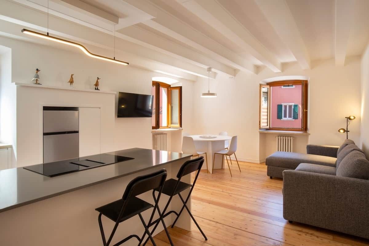 Una cocina moderna con una isla central, un comedor con mesa y sillas, un sofá y un televisor montado en la pared.