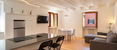 A modern kitchen with a central island, a dining area with a table and chairs, a sofa, and a TV mounted on the wall.