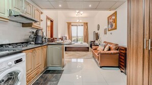 Cocina compacta con lavadora, zona de comedor con sofá y una cama al fondo.