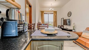Una cocina moderna con cafetera, un comedor con sillas, un sofá, un televisor y un balcón con cortinas.