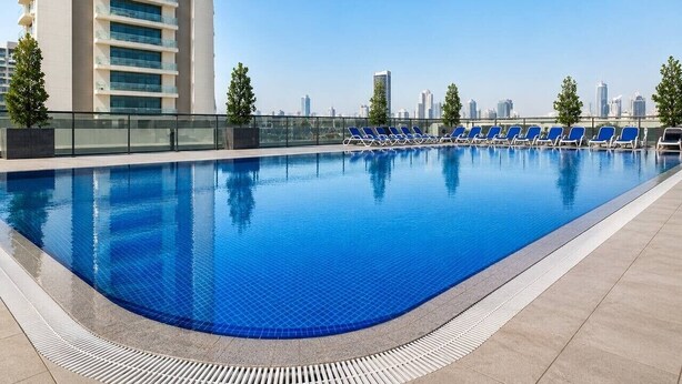 Una piscina en la azotea con sillones de descanso, un edificio alto y un cielo despejado.