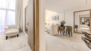 Moderni hotellihuone, jossa on sohva, ruokapöytä tuoleineen, peili ja näkymä ovesta.
