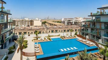 A modern hotel with a rooftop pool, multiple balconies, and a view of the city skyline.