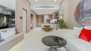 Un salon moderne avec un téléviseur à écran plat, une table basse ronde et un canapé blanc agrémenté d’un coussin rouge.