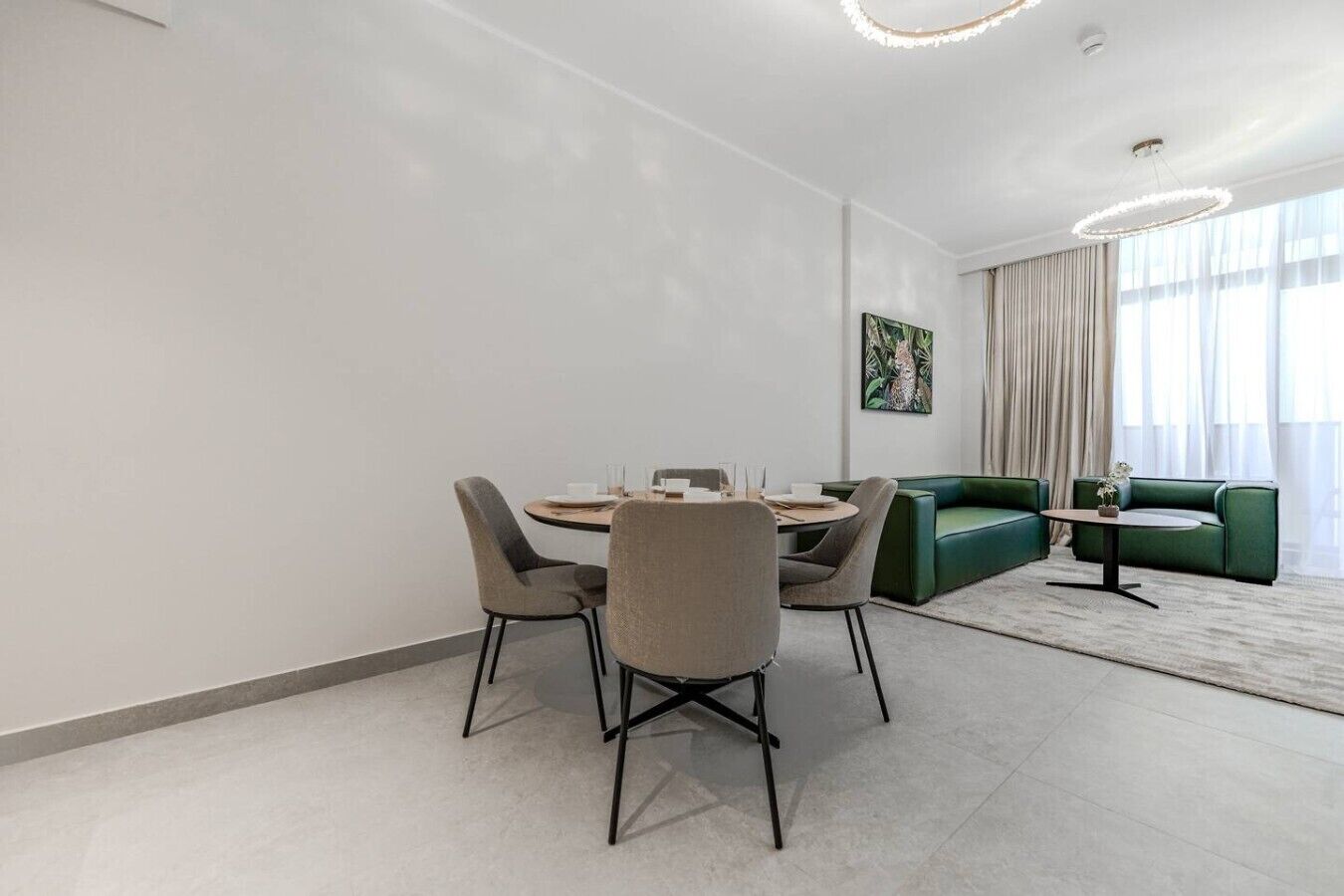 A modern living room with a round table, four chairs, a green sofa, and a painting on the wall.