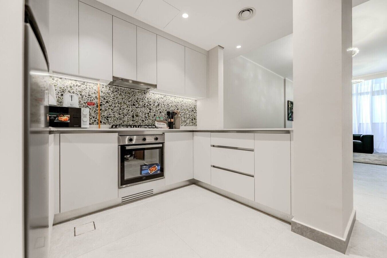 Een moderne keuken met witte kastjes, een ingebouwde oven en een spatwand met een puntpatroon.