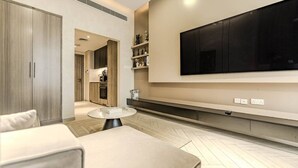 Una sala moderna con una amplia televisión de pantalla plana montada en la pared, una mesa redonda de centro y un sofá.