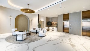 Un vestíbulo moderno con suelo de mármol, sofás blancos, una mesa redonda y un gran aplique de pared.